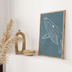 there is a framed whale drawing on the wall next to a vase with some dry grass