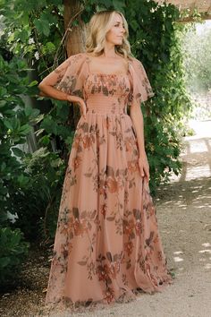 a woman standing in front of a tree wearing a dress with floral print on it