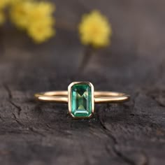 a gold ring with an emerald colored stone in the center on a piece of wood