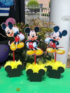 three mickey mouse cupcakes on top of a green table with yellow and red decorations