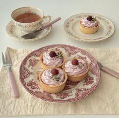 three small cupcakes with whipped cream and strawberries sit on a plate next to a teacup