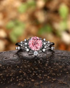 a pink diamond ring sitting on top of a piece of rock with leaves in the background