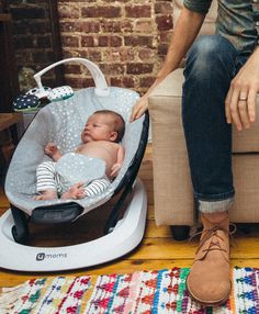 a man sitting on a couch next to a baby in a bouncer