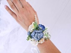 a woman's hand wearing a blue and white wrist corsage with flowers on it