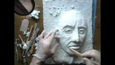 a person that is working on a clay face in the shape of a man's head