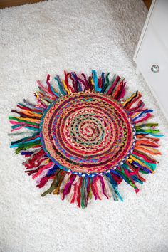 a multicolored round rug on the floor next to a white cabinet and drawer