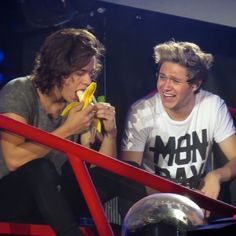 two young men sitting next to each other eating bananas