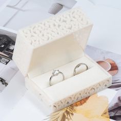 an open box with two wedding rings in it sitting on a table next to other items