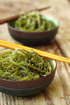 two bowls filled with green noodles next to chopsticks on a wooden table top