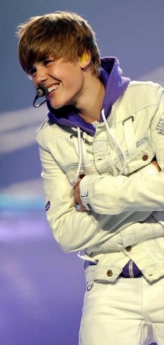 a male in a white jacket and purple hoodie on stage with his arms crossed