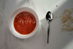 a bowl of soup with the word hello written on it and a spoon next to it