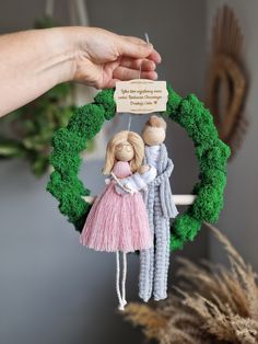 a person holding a small doll in front of a wreath with two people hanging from it