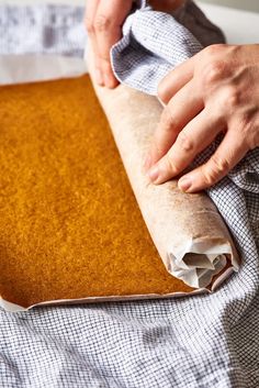 a person is holding a piece of bread on a sheet of paper and wrapping it with a napkin