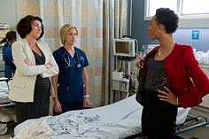 three women standing around a hospital bed talking to one woman in the middle of the room