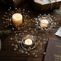 two candles sitting on top of a wooden table next to a book and christmas decorations