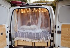 the back end of a van with a bed in it's cargo area and lights hanging from the ceiling