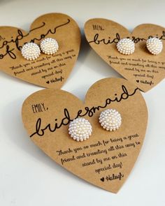 three heart shaped earrings with white pearls on the backs and words written in black ink