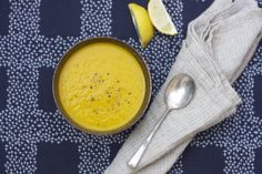 there is a bowl of soup on the table next to a spoon and lemon wedges