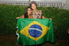 a man and woman holding a brazil flag in front of a hedged garden area