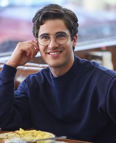 a man sitting at a table with food in front of him and smiling for the camera