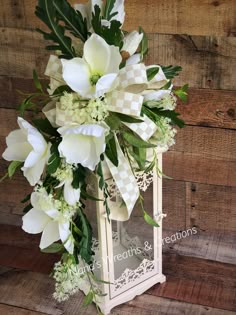 white flowers and greenery are arranged in an old - fashioned glass vase on a wooden background