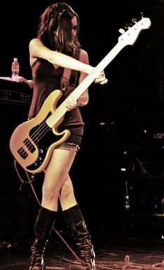 a woman in short shorts and boots holding a bass guitar while standing on a stage