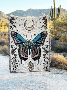 a blanket with a blue butterfly on it in the middle of a desert area next to a cactus