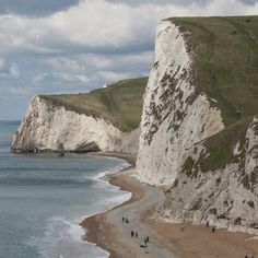 people are walking along the beach near white cliffs