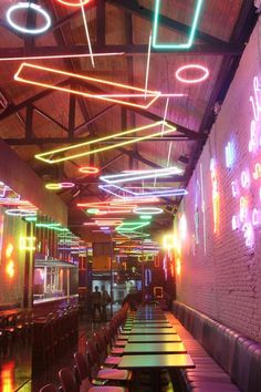 an empty restaurant with neon lights hanging from the ceiling and long tables lined up along the wall