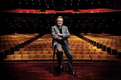 a man sitting on a chair in front of an empty auditorium with rows of seats