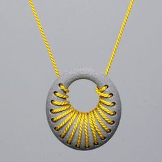 a yellow and gray necklace with an intricate design on the front, hanging from a gold - plated chain