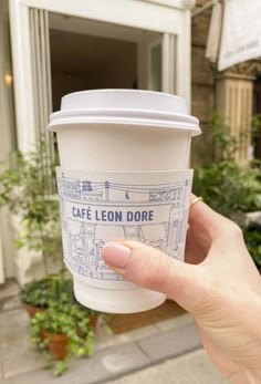 a person holding up a coffee cup with the words cafe leon dore on it