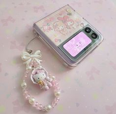 a cell phone with a hello kitty charm attached to it's side next to a bracelet