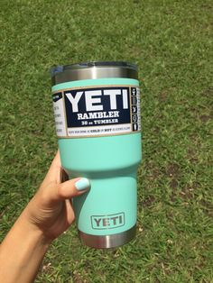 a person holding a yeti tumbler cup in their hand on the green grass