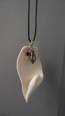 a white flower shaped pendant hangs from a black cord with a red bead on it