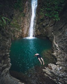 a man diving into a pool in front of a waterfall