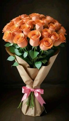 a bouquet of orange roses wrapped in brown paper with a pink bow on the end