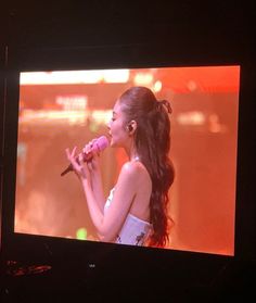 a woman holding a microphone in front of a tv screen with an image on it