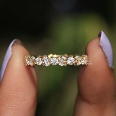 a woman's hand holding a gold ring with five diamonds on it and two fingers