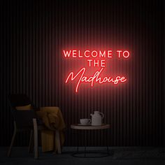 a neon sign that reads welcome to the madhouse with a teapot on a table