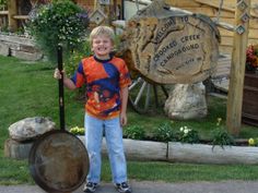 a young boy standing next to a wooden sign holding a stick and an old barrel