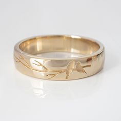 a gold wedding ring with a bird on the tree branch inlayed to it