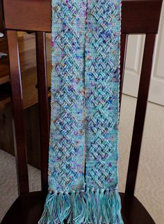 a crocheted scarf sitting on top of a wooden chair next to a table