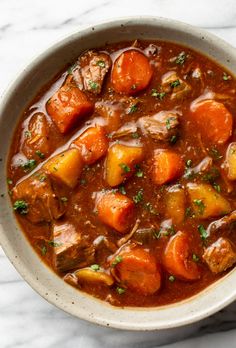 a bowl filled with stew and carrots on top of a marble countertop next to a spoon