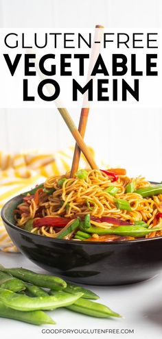 a black bowl filled with noodles and vegetables on top of a white table next to green beans