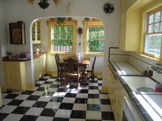 a kitchen with black and white checkered flooring, yellow cabinets and two windows