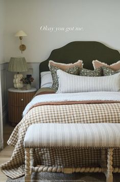 a bed with pillows and blankets on top of it next to a night stand in the corner