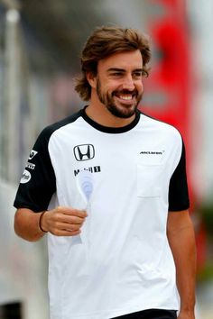 a man with long hair and beard wearing a black and white t - shirt smiles as he walks down the street