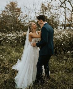 a bride and groom standing in the middle of some tall grass with their arms around each other