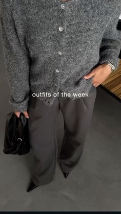 a woman standing in front of a wooden bench wearing a gray sweater and black pants